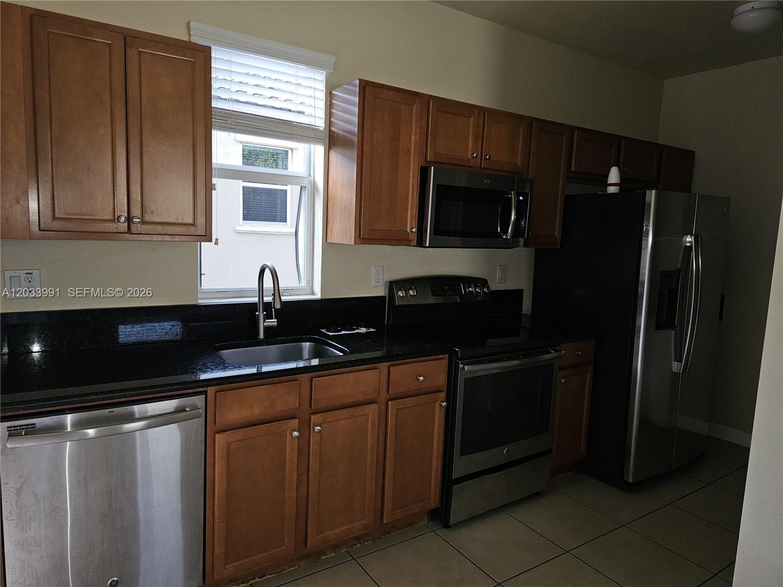A kitchen features wood cabinets, black countertops, stainless steel appliances, and a window above the sink — 17066 SW 95th Ter, Miami FL 33196, MIAMI, FL
