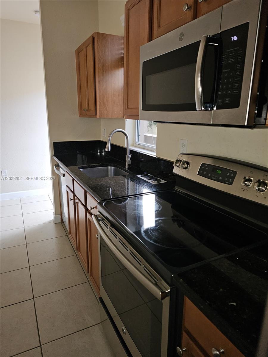 A kitchen features wood cabinets, black countertops, stainless steel appliances, and light-colored floor tiles — 17066 SW 95th Ter, Miami FL 33196, MIAMI, FL