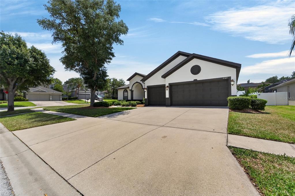 A single-story house with a white exterior, dark trim, and a three-car garage — 2309 SILVER TRUMPET COURT, VALRICO, FL
