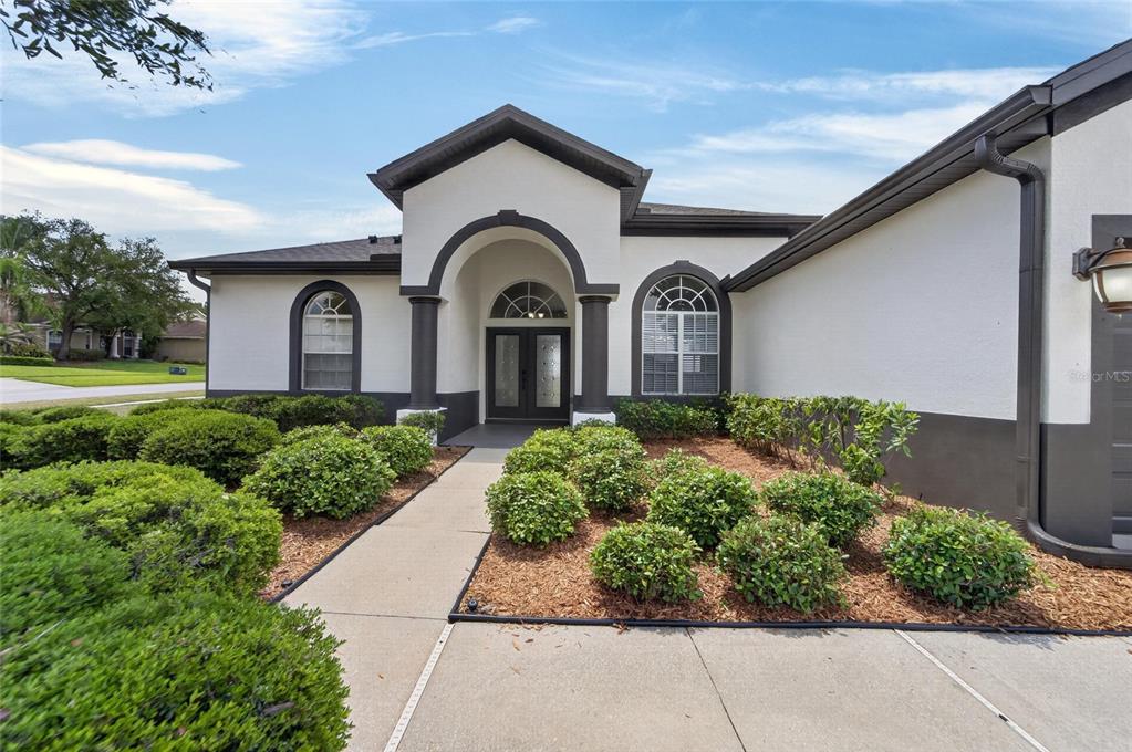 The exterior of a house features a white stucco facade, dark trim, and a walkway — 2309 SILVER TRUMPET COURT, VALRICO, FL