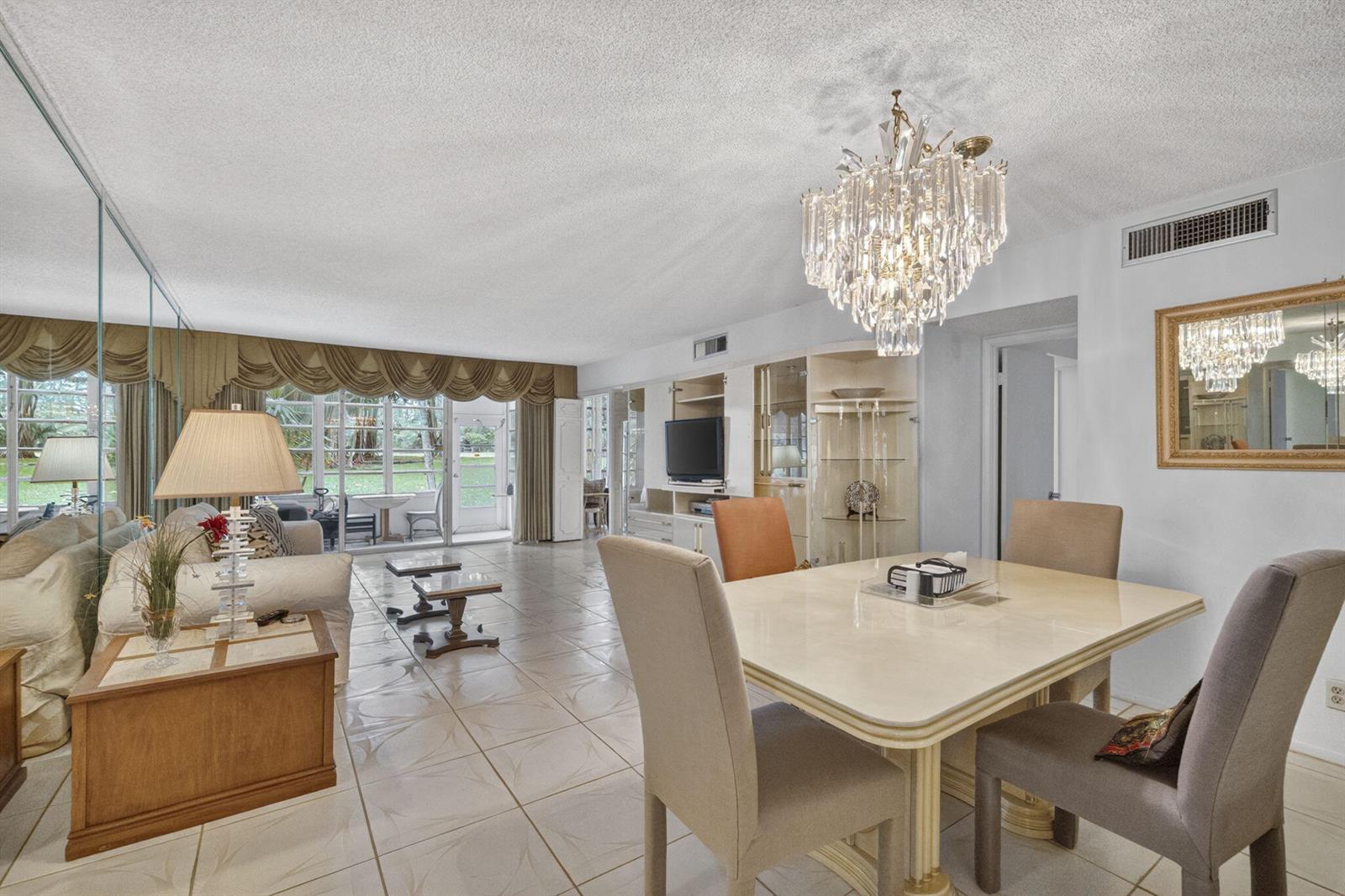 A dining area and living room with tile floors, a crystal chandelier, and mirrored walls — 3000 S Course Drive # 103, Pompano Beach FL 33069, POMPANO BEACH, FL