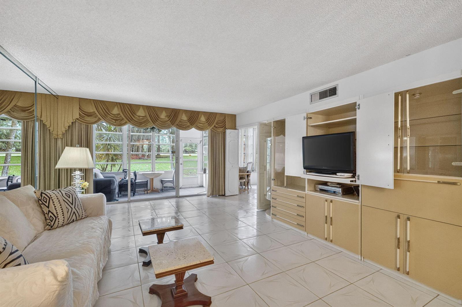 A living room features light tile floors, a large entertainment center, and sliding glass doors — 3000 S Course Drive # 103, Pompano Beach FL 33069, POMPANO BEACH, FL