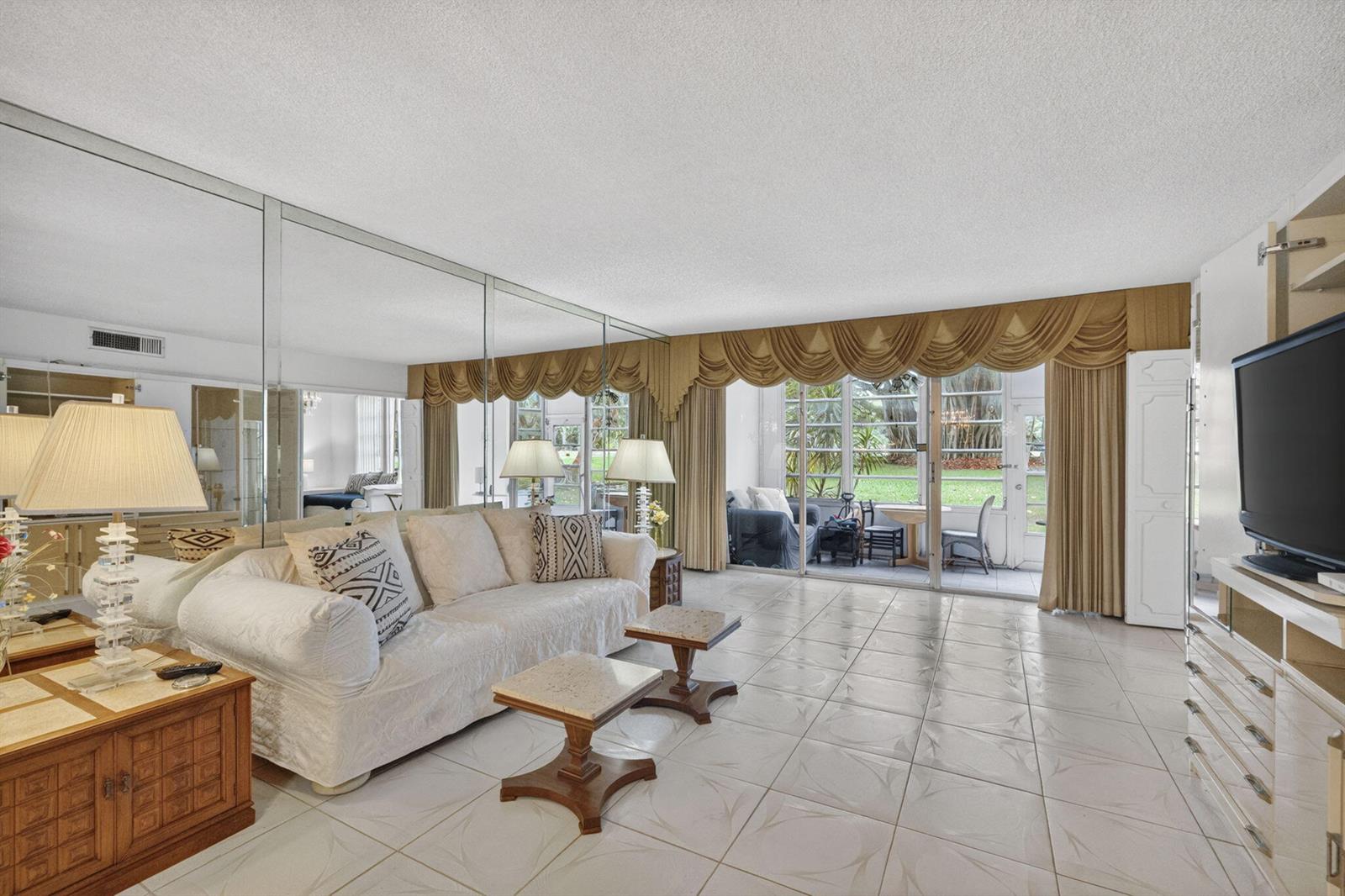 A living room with tiled floors, a mirrored wall, and sliding glass doors to a patio — 3000 S Course Drive # 103, Pompano Beach FL 33069, POMPANO BEACH, FL