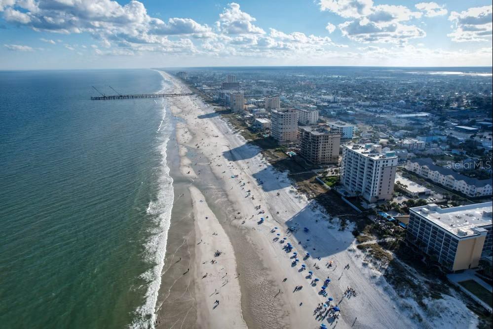 An aerial view shows a sandy beach, ocean waves, a fishing pier, and coastal high-rises — 6 N BEACH WAY, JACKSONVILLE BEACH, FL