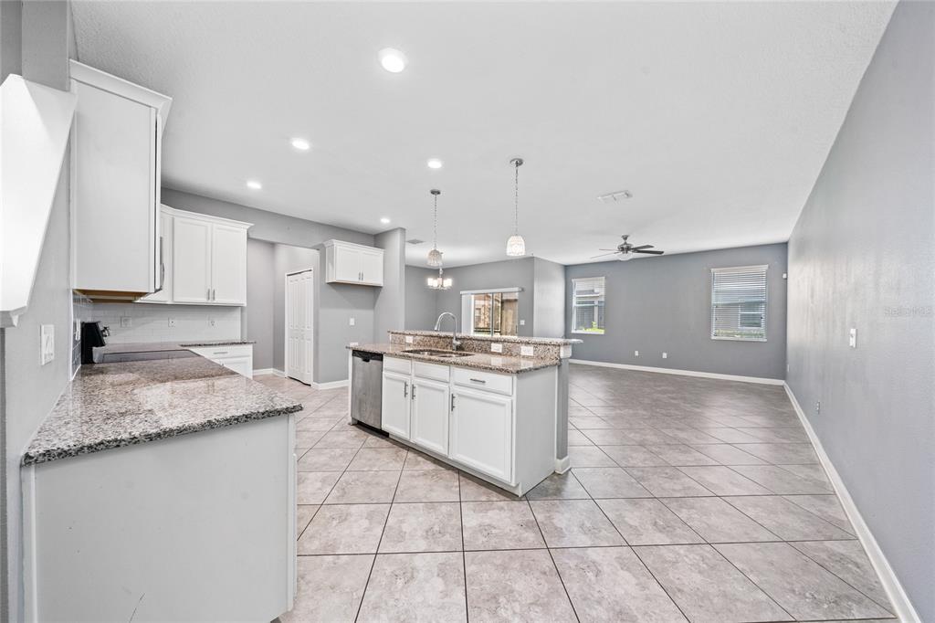 A kitchen with white cabinets, granite countertops, and an island opens to a living area — 15215 PACEY COVE DRIVE, ORLANDO, FL
