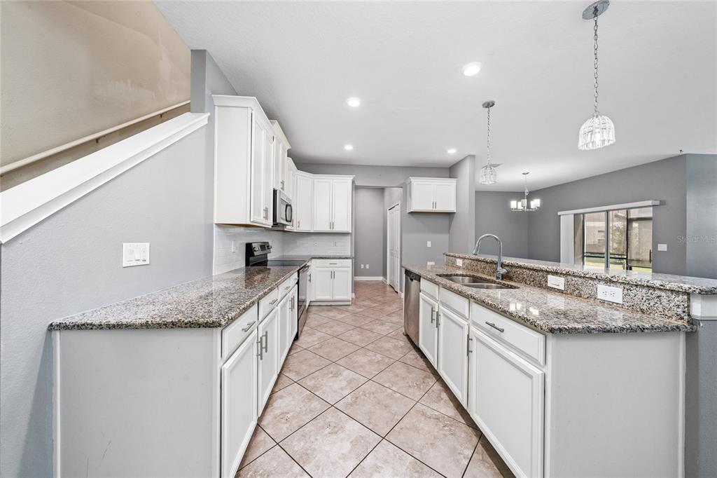 A kitchen with white cabinets, granite countertops, and tile flooring opens to a dining area — 15215 PACEY COVE DRIVE, ORLANDO, FL