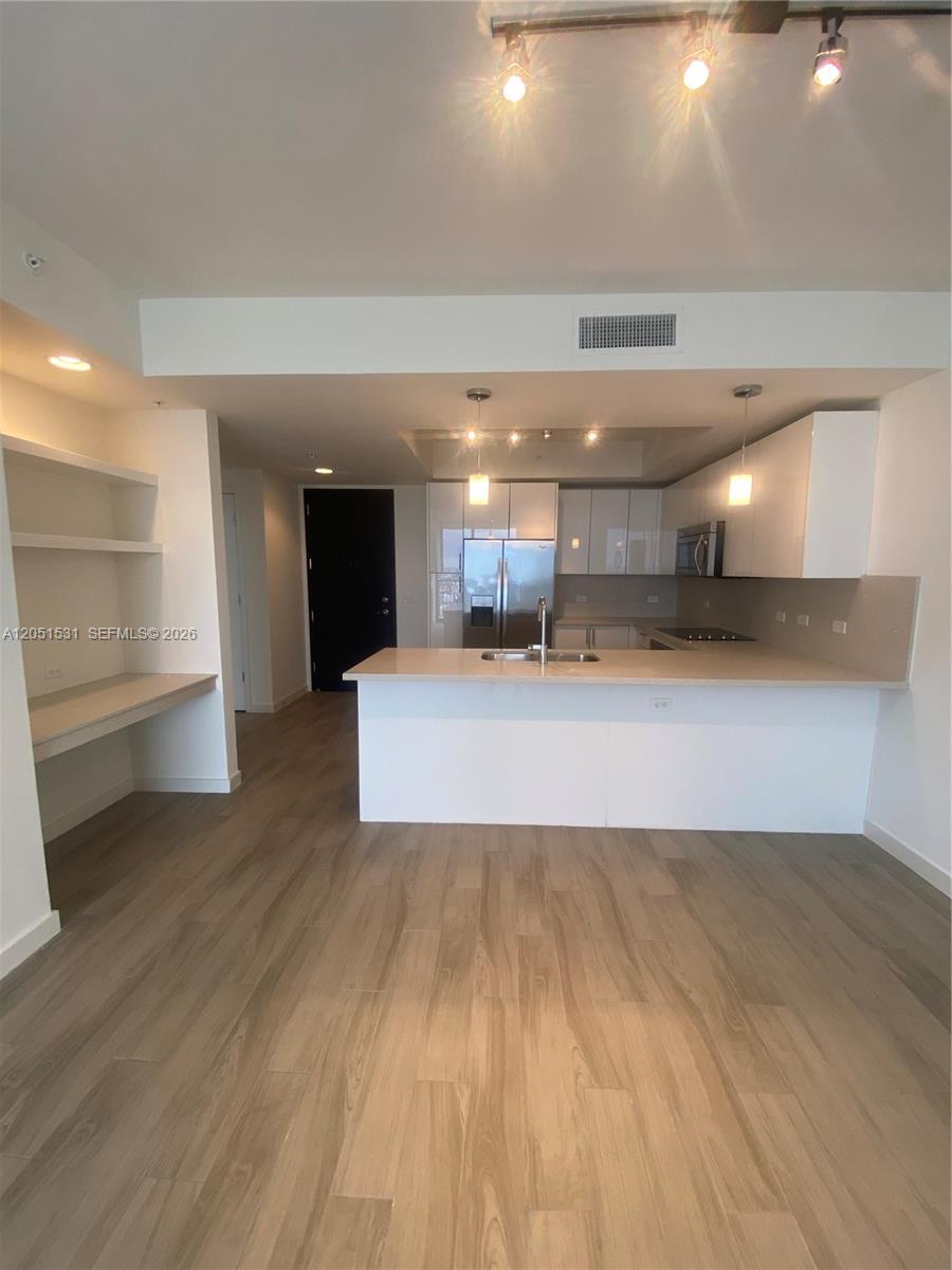 A modern kitchen features white cabinetry, a breakfast bar, and light wood-look flooring — 999 SW 1 AVE # 3209, Miami FL 33130, MIAMI, FL