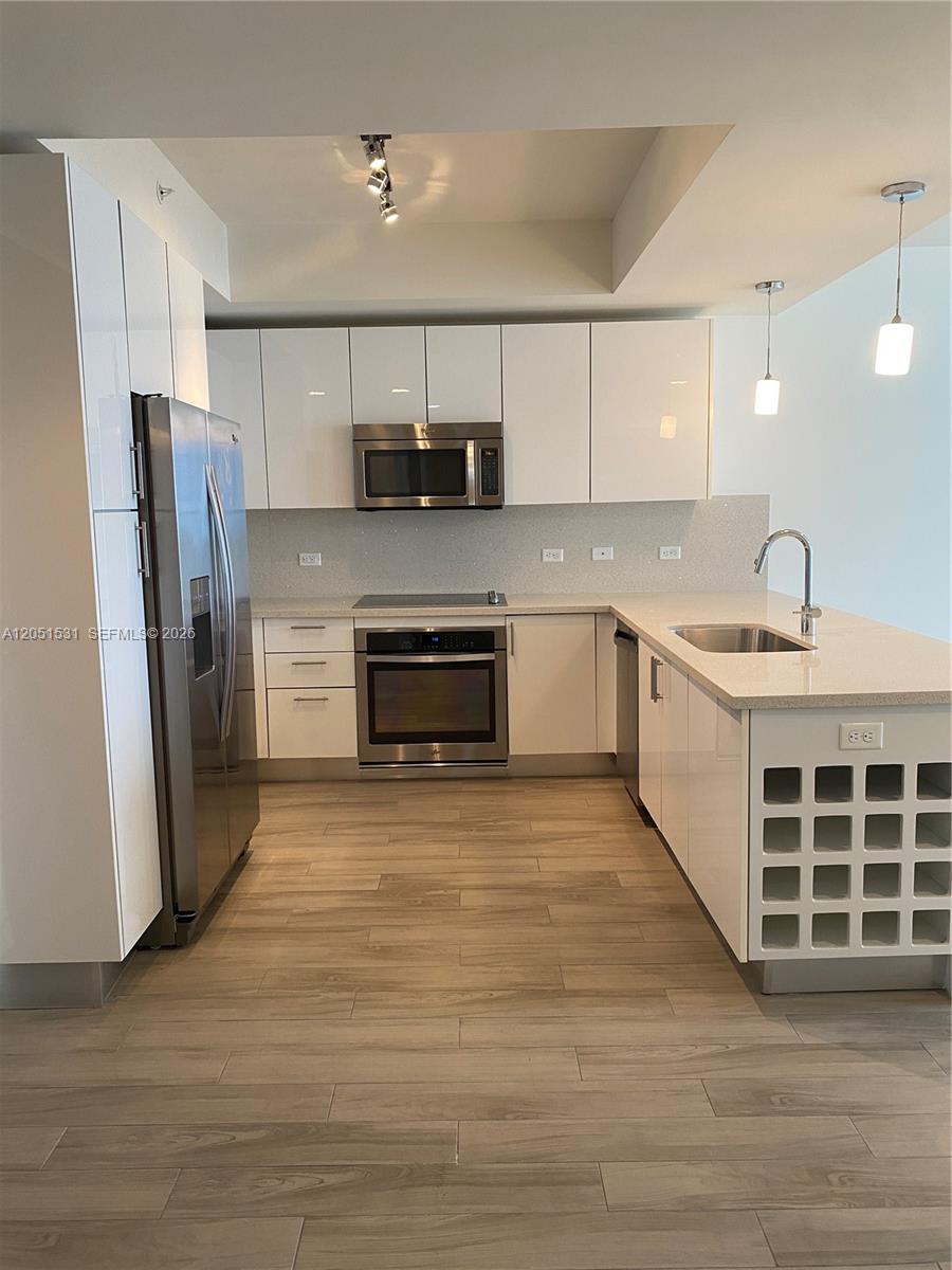 A modern kitchen features white cabinets, stainless steel appliances, and light wood-look flooring — 999 SW 1 AVE # 3209, Miami FL 33130, MIAMI, FL