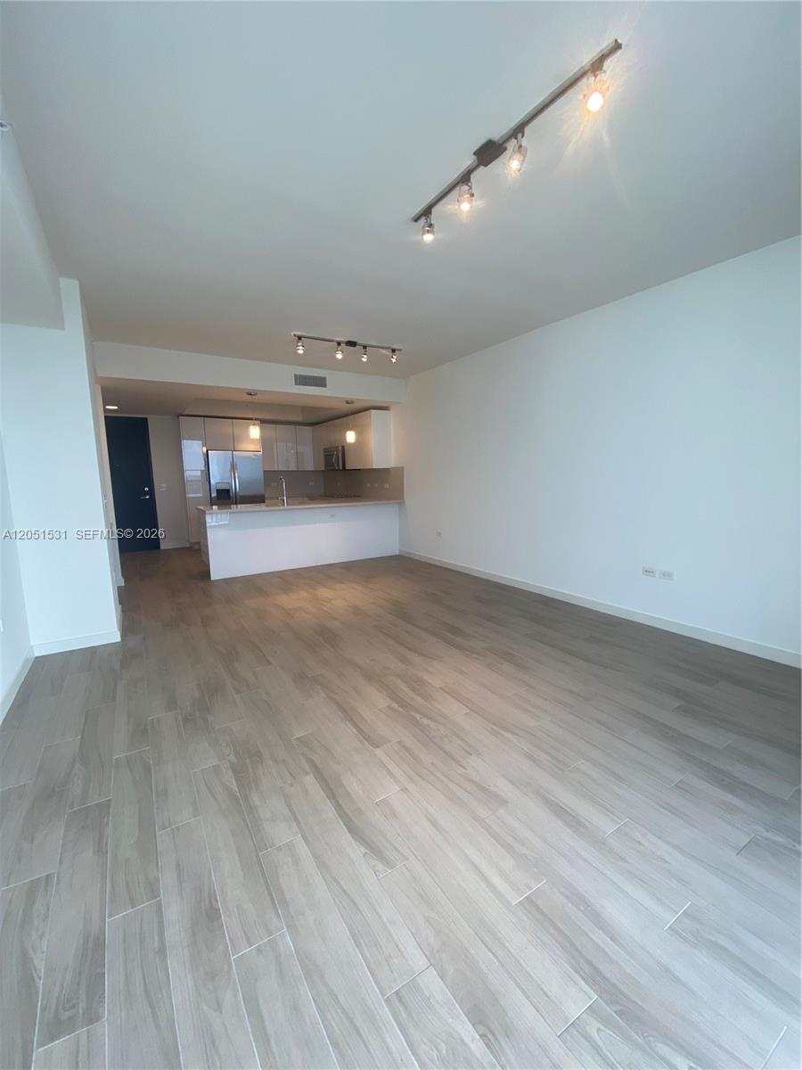 An open-concept living area features light wood-look tile flooring and a kitchen with white cabinetry — 999 SW 1 AVE # 3209, Miami FL 33130, MIAMI, FL