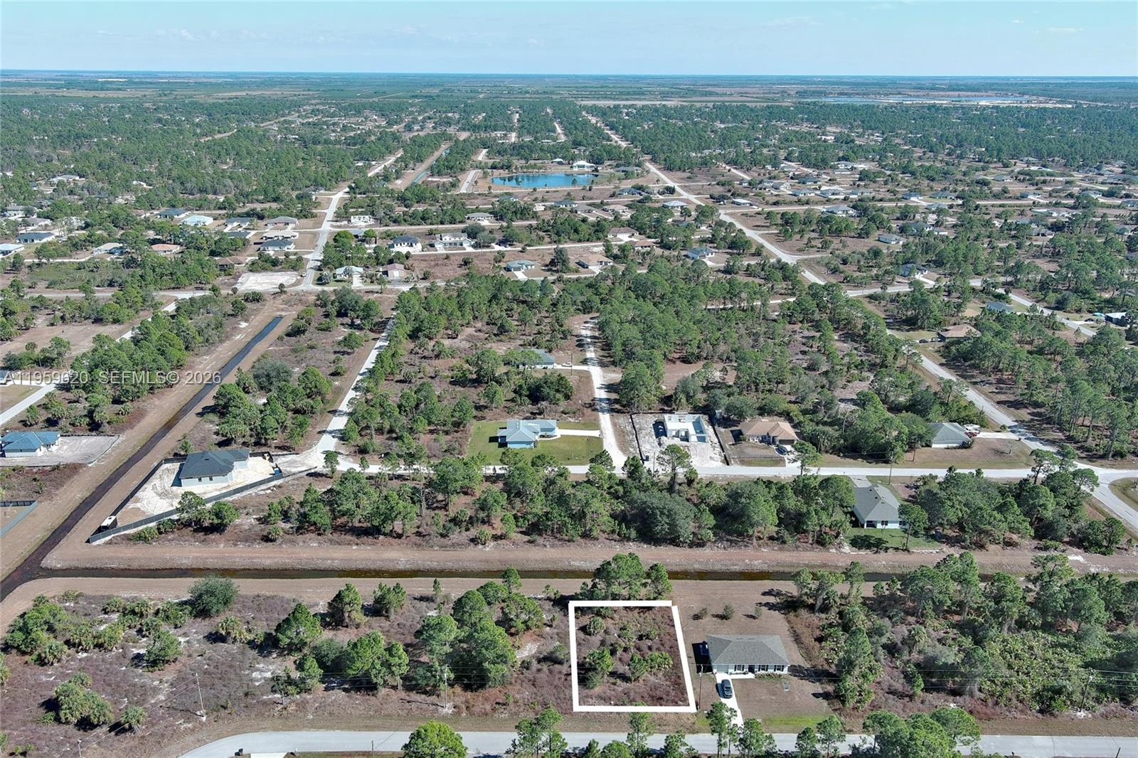 An aerial view shows a vacant rectangular lot outlined in white next to a house — 943 FOXDALE AVE, Lehigh Acres FL 33974, LEHIGH ACRES, FL
