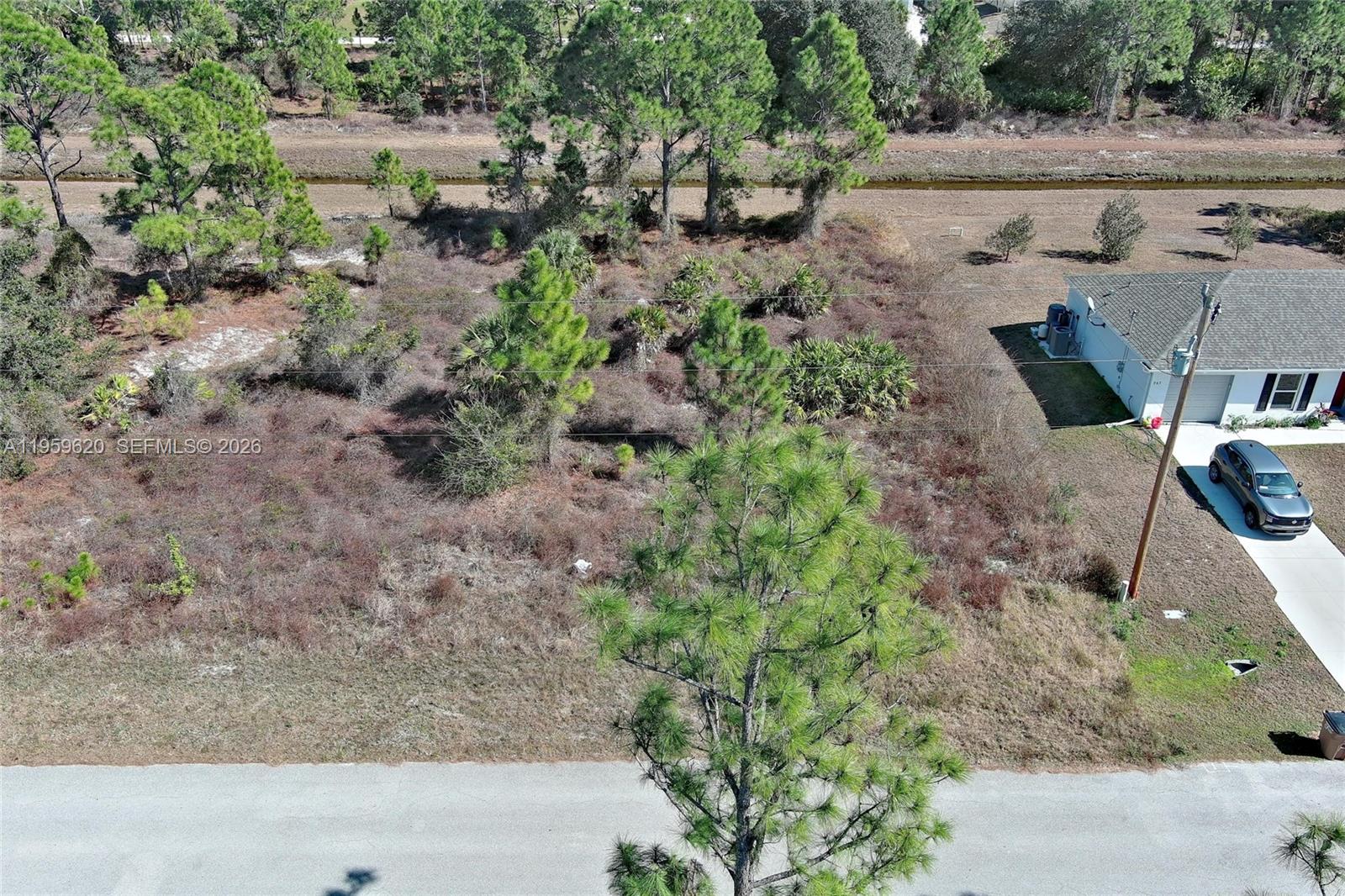 An aerial view shows a vacant, wooded residential lot next to a house and driveway — 943 FOXDALE AVE, Lehigh Acres FL 33974, LEHIGH ACRES, FL