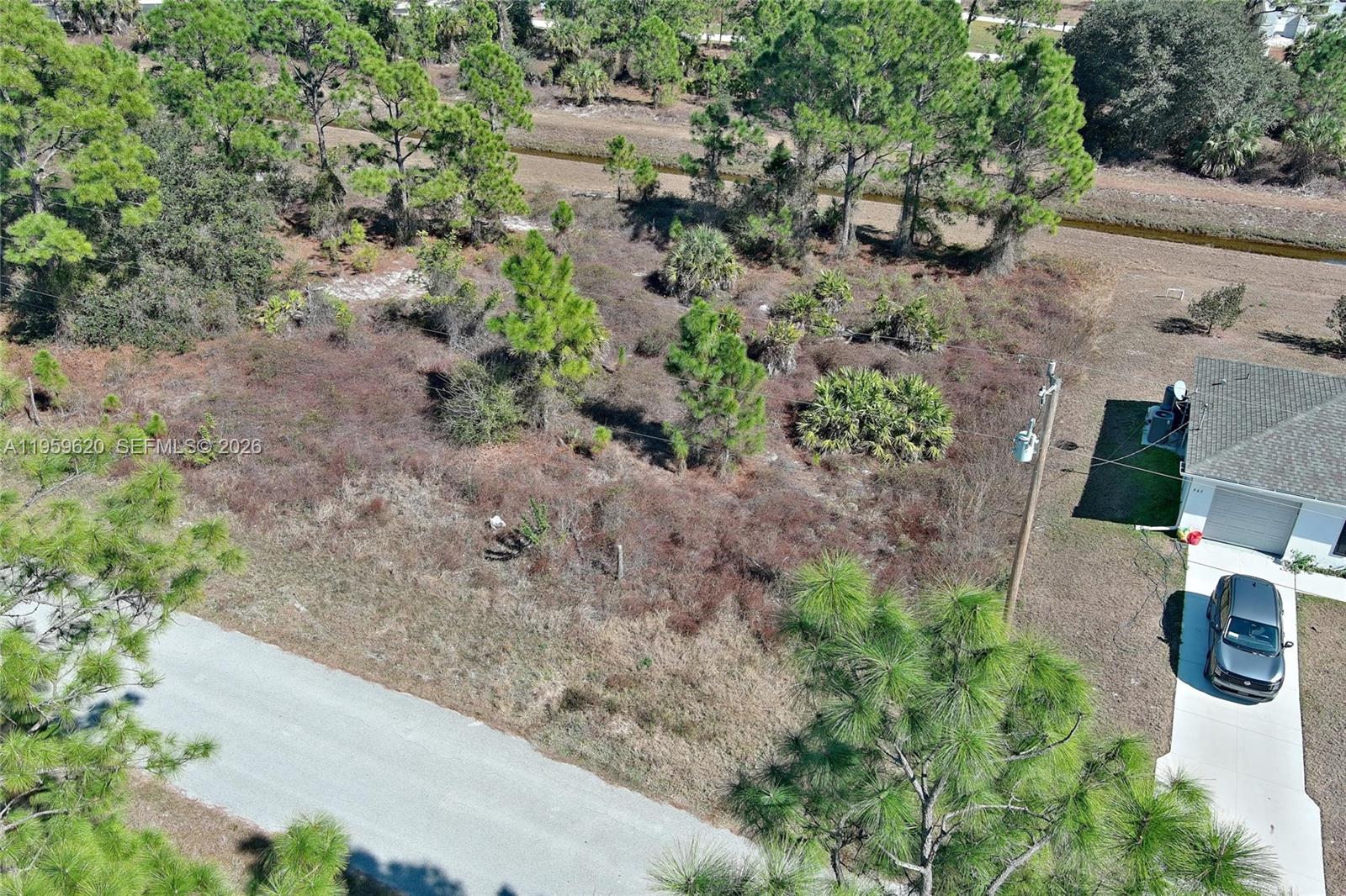 An aerial view shows a vacant, wooded lot situated next to a house and driveway — 943 FOXDALE AVE, Lehigh Acres FL 33974, LEHIGH ACRES, FL