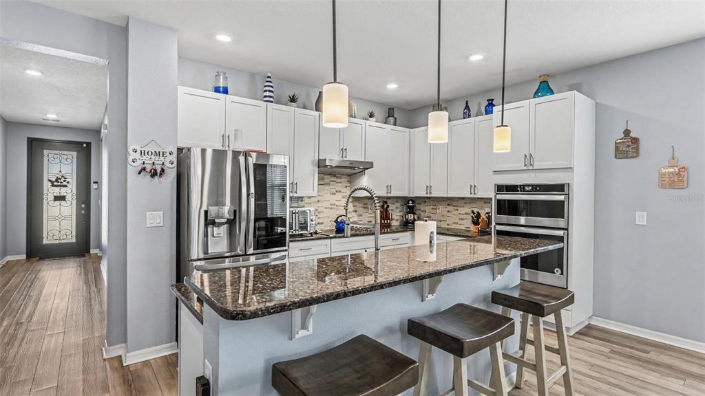 A kitchen features white cabinets, granite countertops, stainless steel appliances, and a breakfast bar — 7589 MUSCOVY DRIVE, LAKELAND, FL