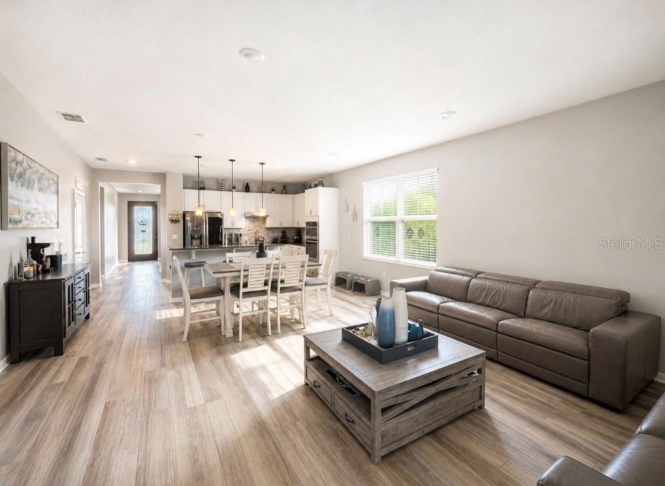 An open-concept living room and kitchen featuring light wood flooring and a grey leather sofa — 7589 MUSCOVY DRIVE, LAKELAND, FL