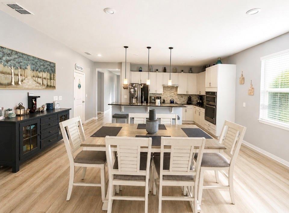 A dining area with a wooden table and white chairs sits before an open kitchen — 7589 MUSCOVY DRIVE, LAKELAND, FL