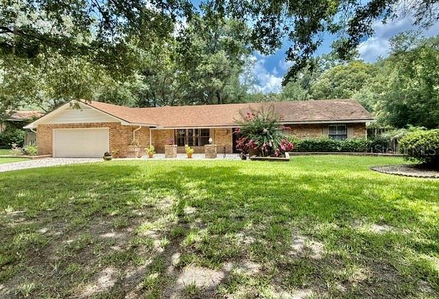 A single-story brick house with a large lawn and mature trees under a cloudy sky — 543 PRINCEWOOD DRIVE, DELAND, FL