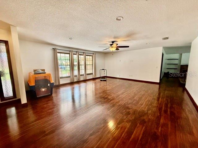 A spacious living room features dark wood flooring, a ceiling fan, and large windows — 543 PRINCEWOOD DRIVE, DELAND, FL