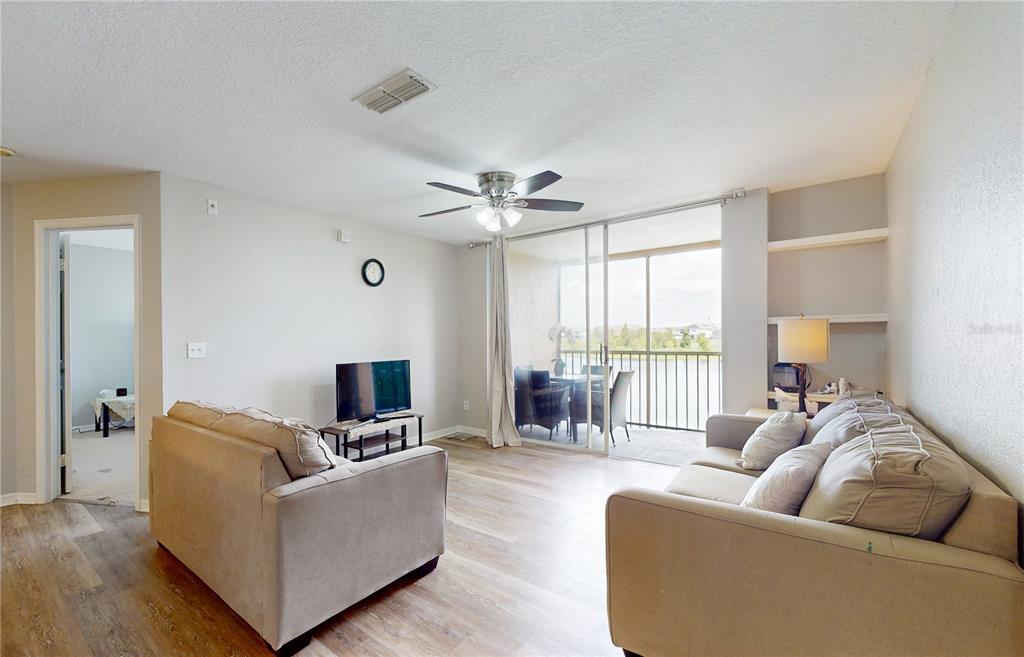 A living room with light wood flooring, two sofas, a ceiling fan, and a balcony view — 8801 LATREC AVENUE UNIT 8208, ORLANDO, FL