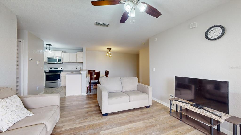 A living room with light wood-look flooring, a beige loveseat, and an open kitchen — 8801 LATREC AVENUE UNIT 8208, ORLANDO, FL
