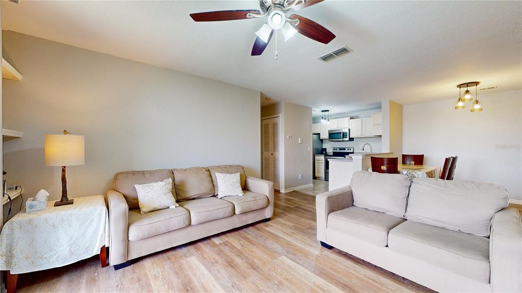 A living room features two beige sofas, wood-look flooring, and an open kitchen beyond — 8801 LATREC AVENUE UNIT 8208, ORLANDO, FL