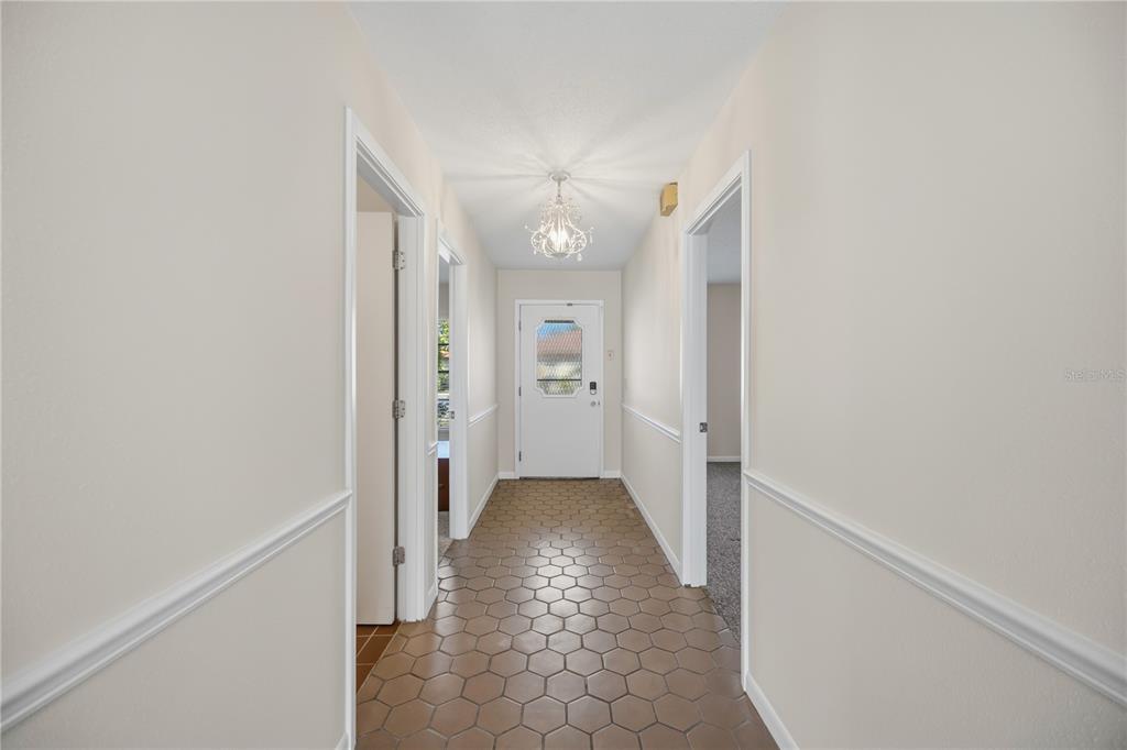 A hallway with hexagonal tile flooring, white walls, chair rail molding, and a front door — 849 SENDA PLATA UNIT 15, VENICE, FL