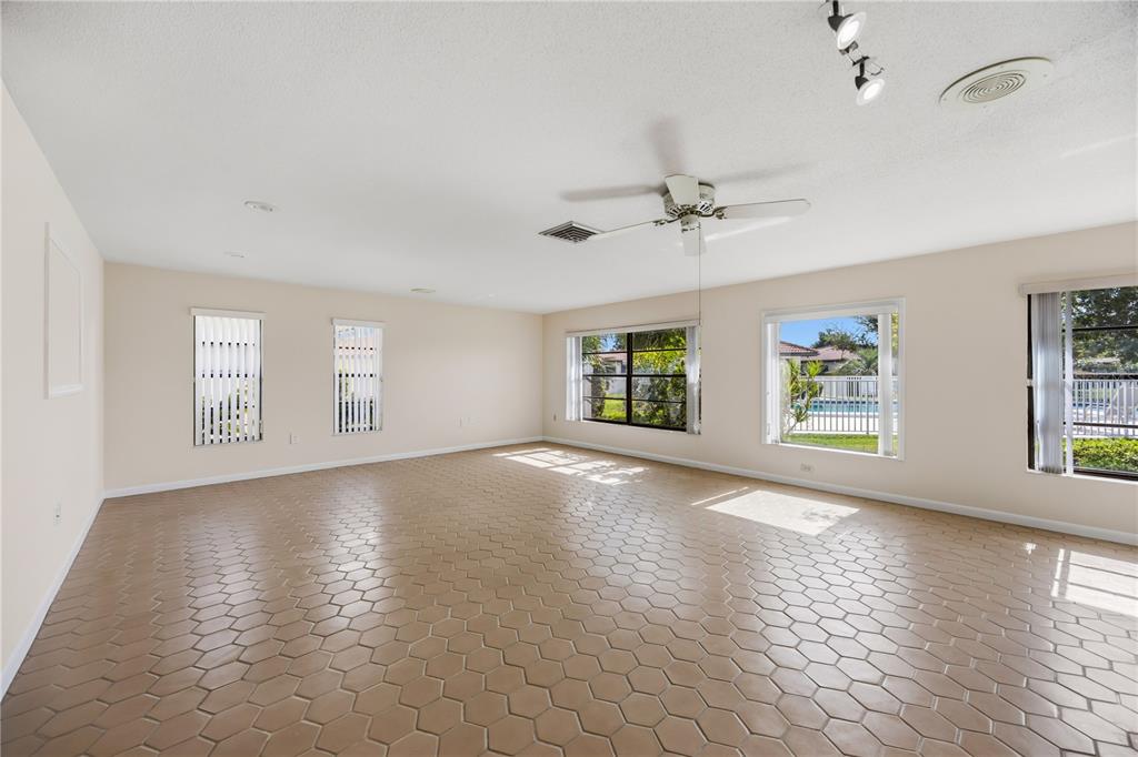 A spacious, empty living room features beige hexagonal tile flooring, a ceiling fan, and windows — 849 SENDA PLATA UNIT 15, VENICE, FL