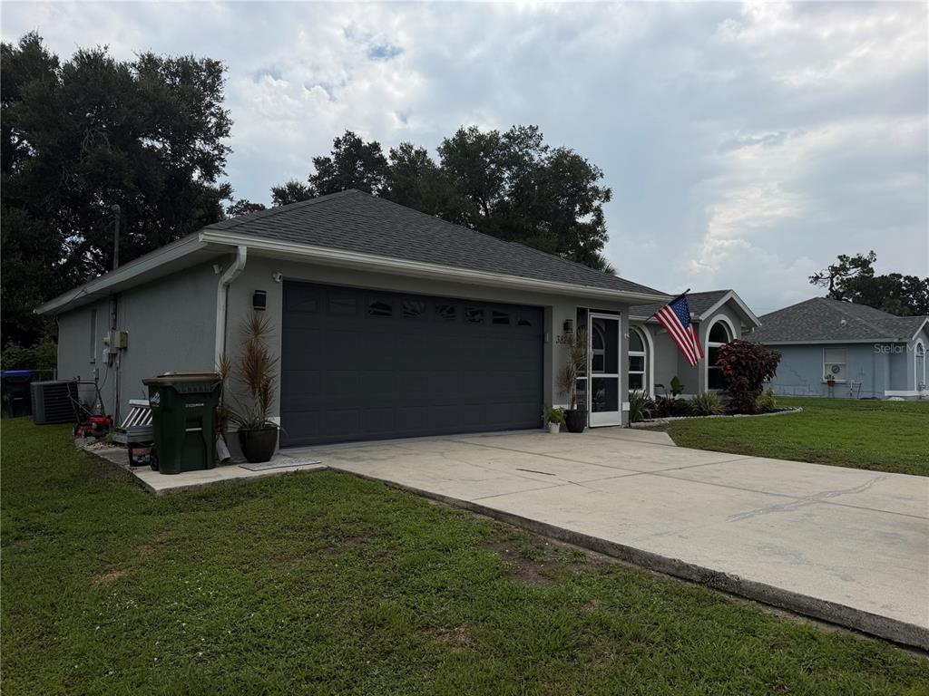A gray single-story house with a dark garage door, concrete driveway, and an American flag — 3824 HOLIN LANE, NORTH PORT, FL