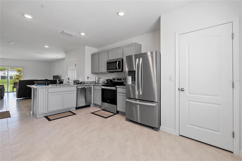 A kitchen with gray cabinets, stainless steel appliances, and tile flooring opens to a living area — 3476 MAJOR OAK BOULEVARD, APOPKA, FL