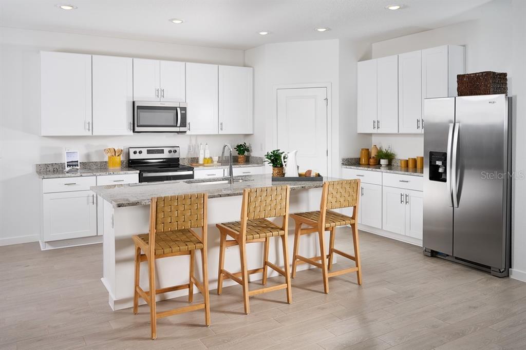 A modern kitchen features white cabinets, granite countertops, stainless steel appliances, and a central island — 82 WANDERING CREEK WAY, PALM COAST, FL