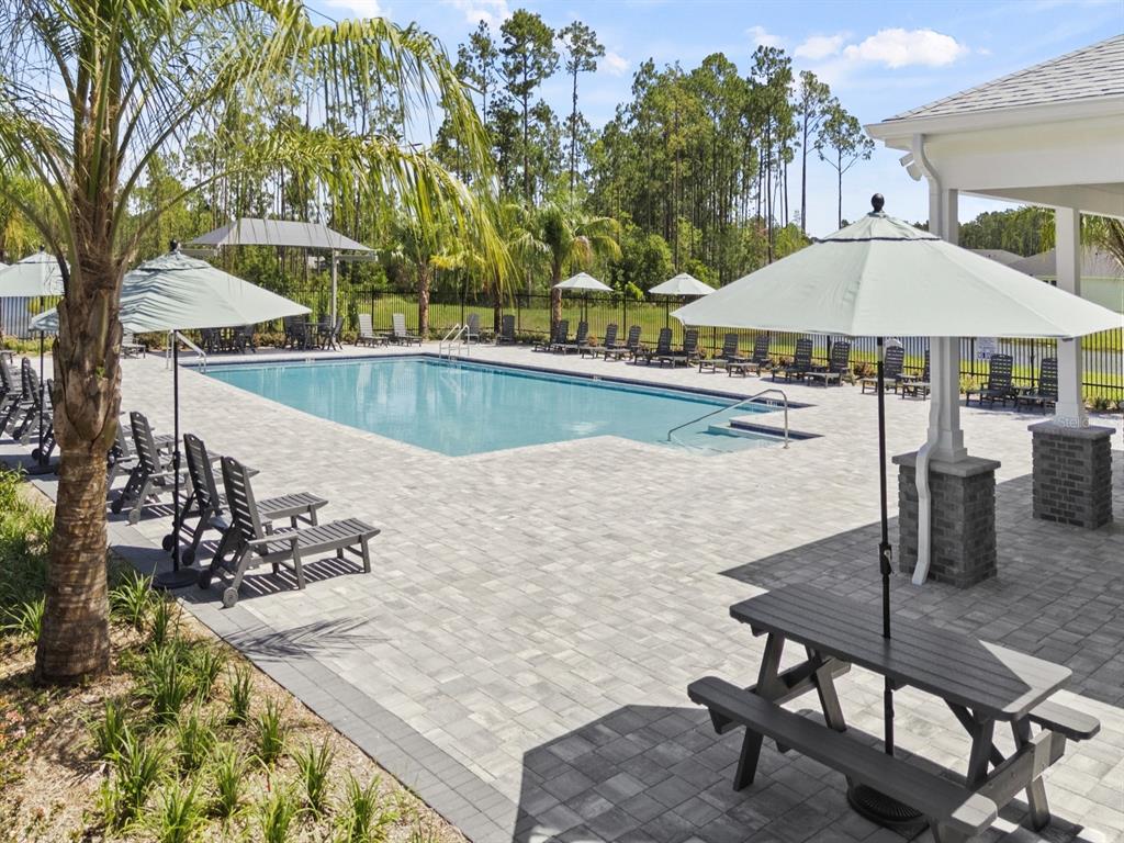 A swimming pool with lounge chairs and umbrellas on a paved deck near a building — 82 WANDERING CREEK WAY, PALM COAST, FL