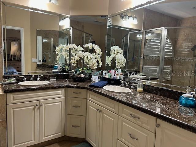 A bathroom features dual sinks, cream-colored cabinetry, and dark marble countertops with large mirrors — 1308 LAKE WILLISARA CIRCLE UNIT 28-12, ORLANDO, FL
