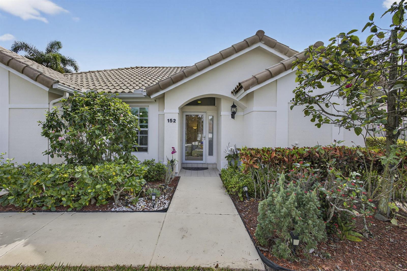 A concrete walkway leads to the front entrance of a single-story home with landscaping — 152 Eagleton Court, Palm Beach Gardens FL 33418, PALM BEACH GARDENS, FL
