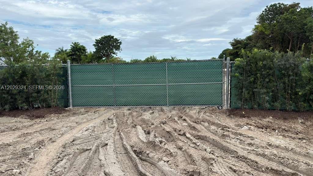 A chain-link gate with a green privacy screen stands in front of a muddy lot — SW 213TH AVE, Miami FL 33187, MIAMI, FL
