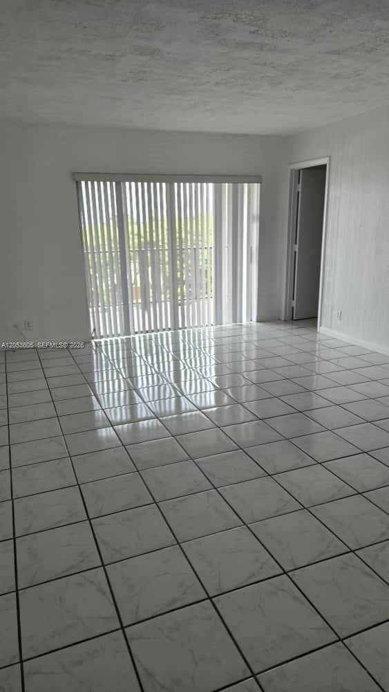 An empty room features white tiled floors, white walls, and a large sliding glass door — 13707 Kendale Lakes Cir, Miami FL 33183, MIAMI, FL