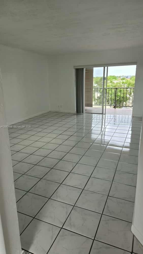 An empty room features white tile flooring and a sliding glass door leading to a balcony — 13707 Kendale Lakes Cir, Miami FL 33183, MIAMI, FL
