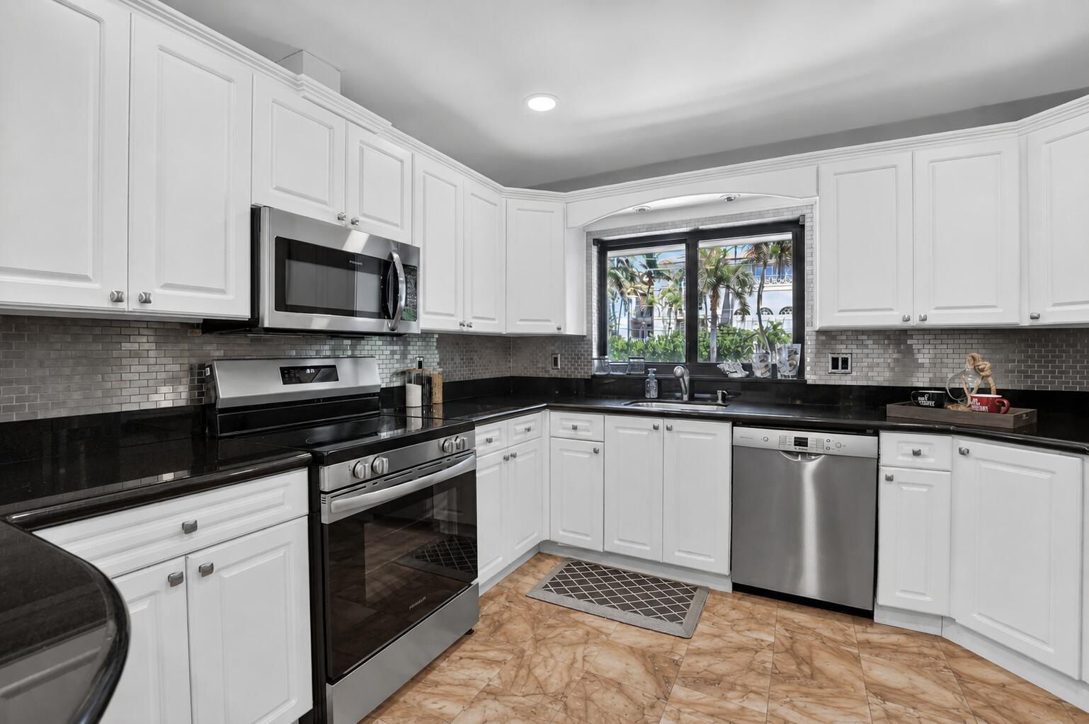 A kitchen with white cabinets, black countertops, stainless steel appliances, and a window overlooking palm trees — 4310 S Ocean Boulevard # B, Highland Beach FL 33487, HIGHLAND BEACH, FL