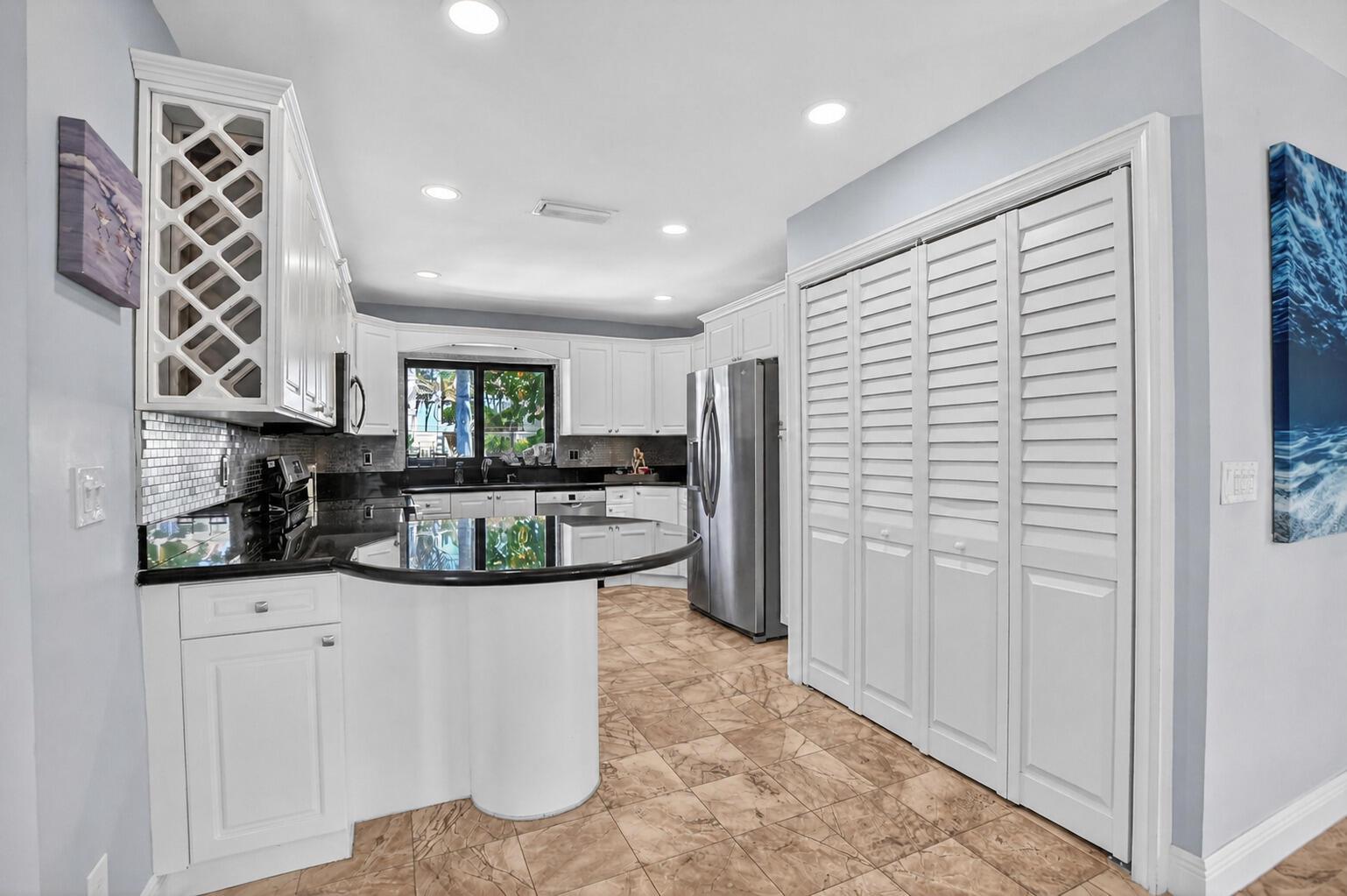 A kitchen features white cabinetry, black countertops, stainless steel appliances, and light-colored tile flooring — 4310 S Ocean Boulevard # B, Highland Beach FL 33487, HIGHLAND BEACH, FL