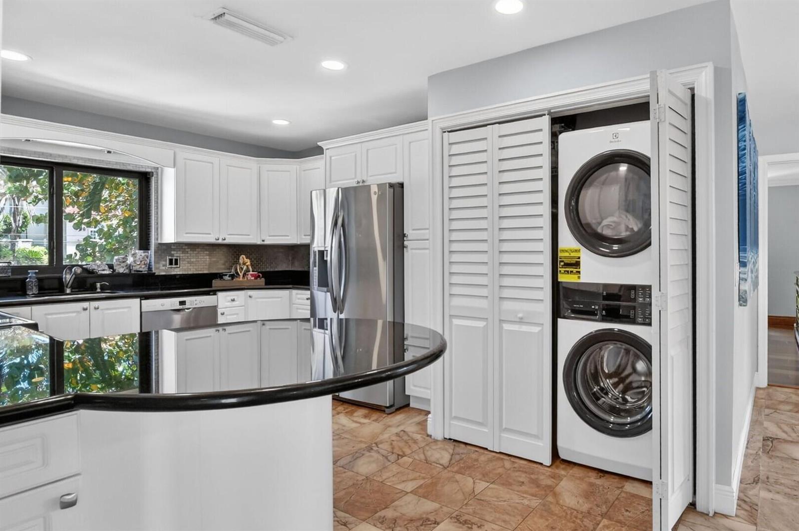 A kitchen with white cabinets, black countertops, and a stacked washer and dryer unit — 4310 S Ocean Boulevard # B, Highland Beach FL 33487, HIGHLAND BEACH, FL