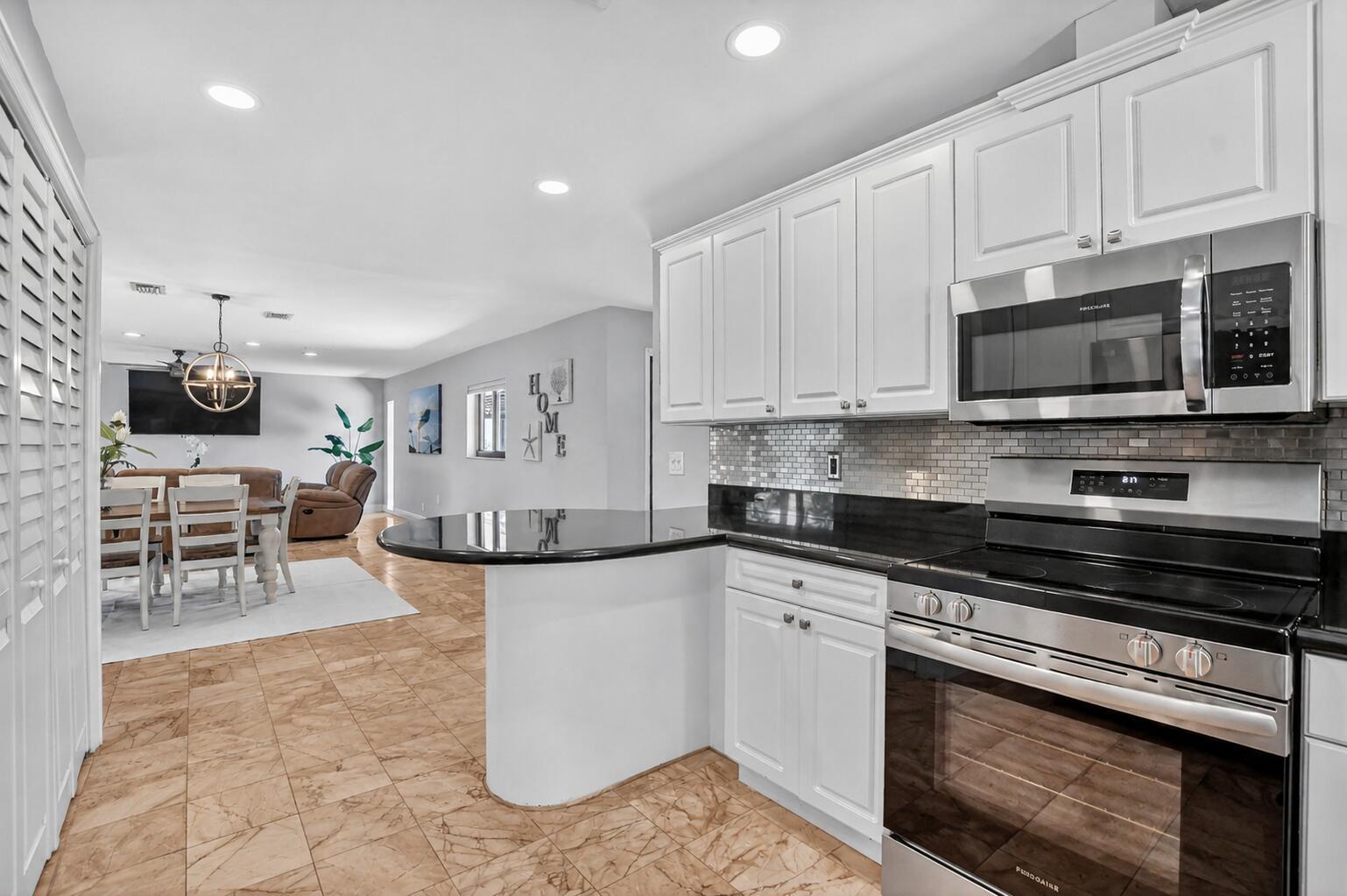 A kitchen with white cabinets, black countertops, and stainless steel appliances opens to a dining area — 4310 S Ocean Boulevard # B, Highland Beach FL 33487, HIGHLAND BEACH, FL