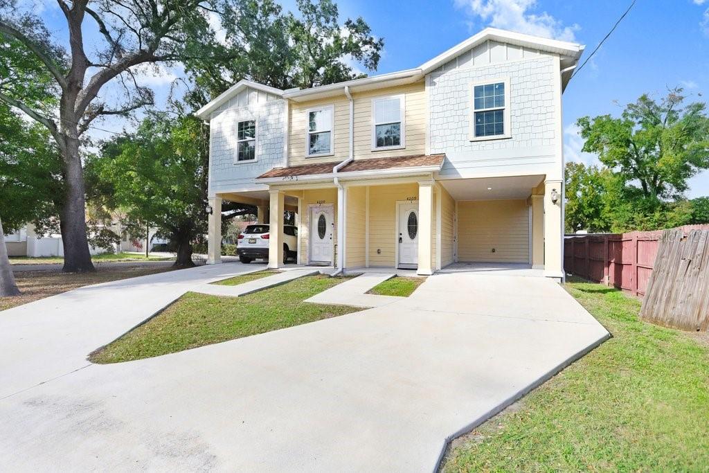 A two-story duplex with yellow siding, covered entryways, and concrete driveways under a blue sky — 4209 W WOODLAWN AVENUE, TAMPA, FL