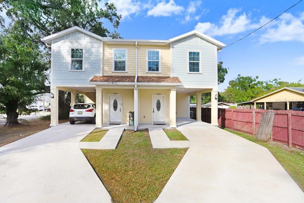 A two-story duplex with yellow siding, white trim, and covered parking spaces on each side — 4209 W WOODLAWN AVENUE, TAMPA, FL