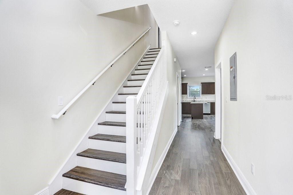 A hallway with wood-look flooring leads to a kitchen, featuring a staircase with white railings — 4209 W WOODLAWN AVENUE, TAMPA, FL