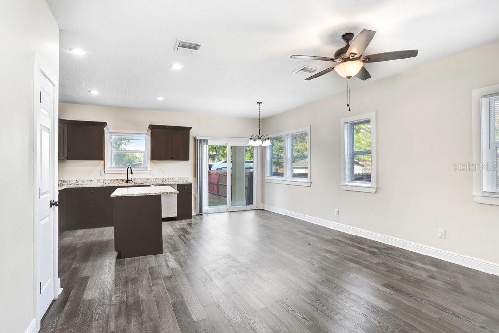An open-concept kitchen and dining area features dark cabinets, granite countertops, and wood-look flooring — 4209 W WOODLAWN AVENUE, TAMPA, FL