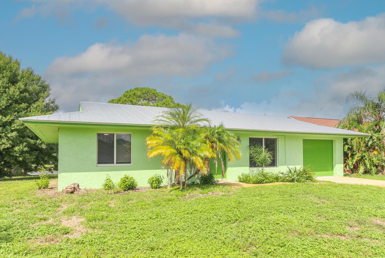 A single-story house with lime green stucco walls, a metal roof, and a front-facing garage — 431 NE Julia Court, Jensen Beach FL 34957, JENSEN BEACH, FL