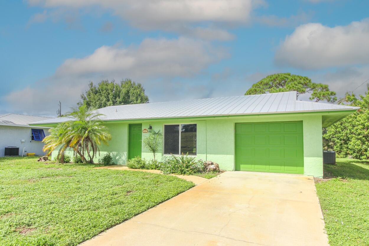 A light green single-story house with a metal roof, attached garage, and concrete driveway — 431 NE Julia Court, Jensen Beach FL 34957, JENSEN BEACH, FL