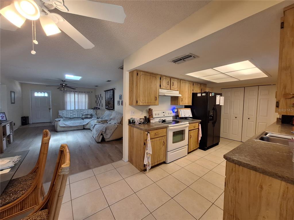 A kitchen with light wood cabinets and tile floors opens into a living room area — 419 FALCON AVENUE, EDGEWATER, FL