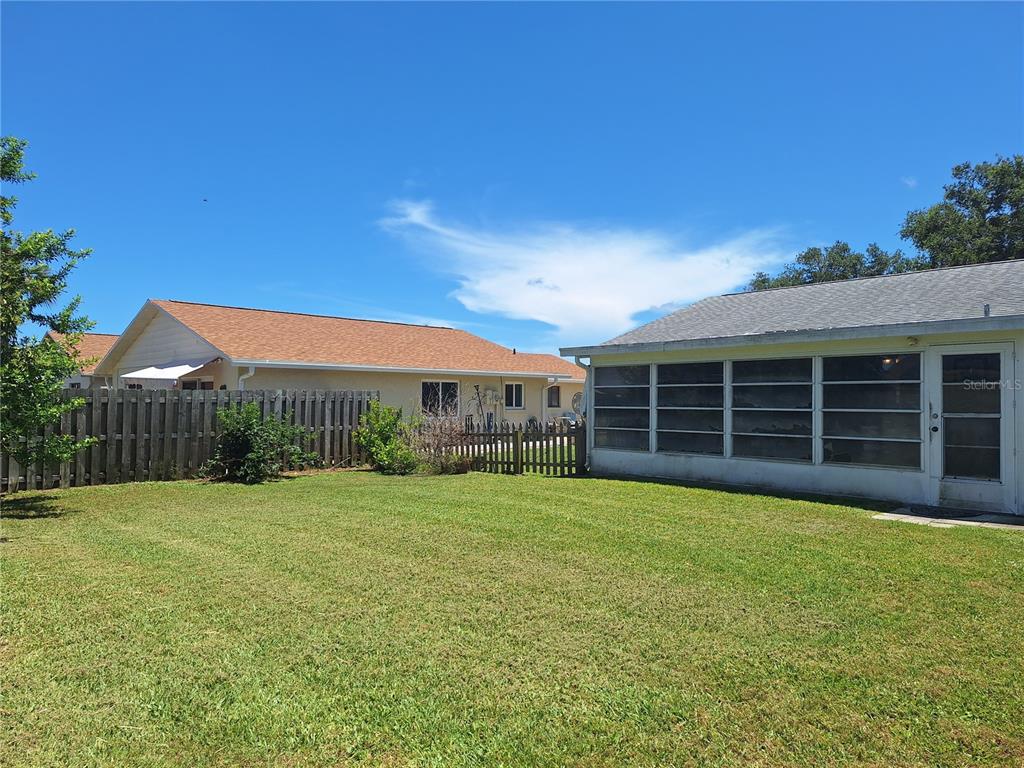 A grassy backyard features a wooden fence and a house with a screened-in porch — 419 FALCON AVENUE, EDGEWATER, FL