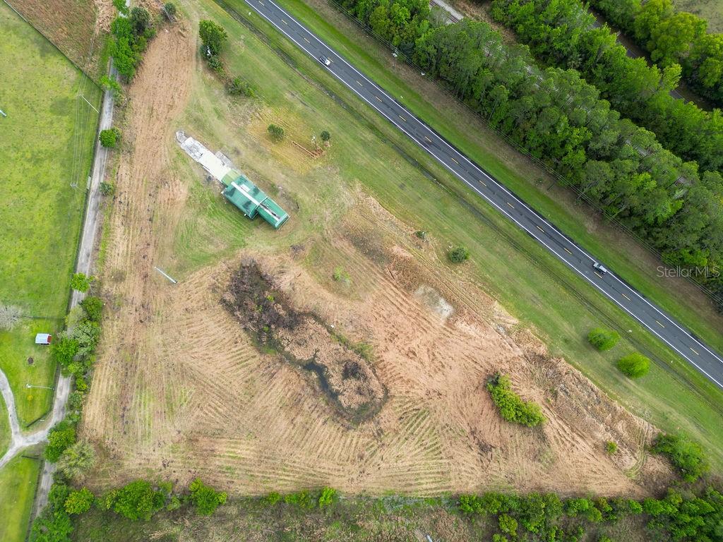 An aerial view shows a cleared, grassy lot with a small structure and a nearby highway — 6029 US HIGHWAY 17, DE LEON SPRINGS, FL