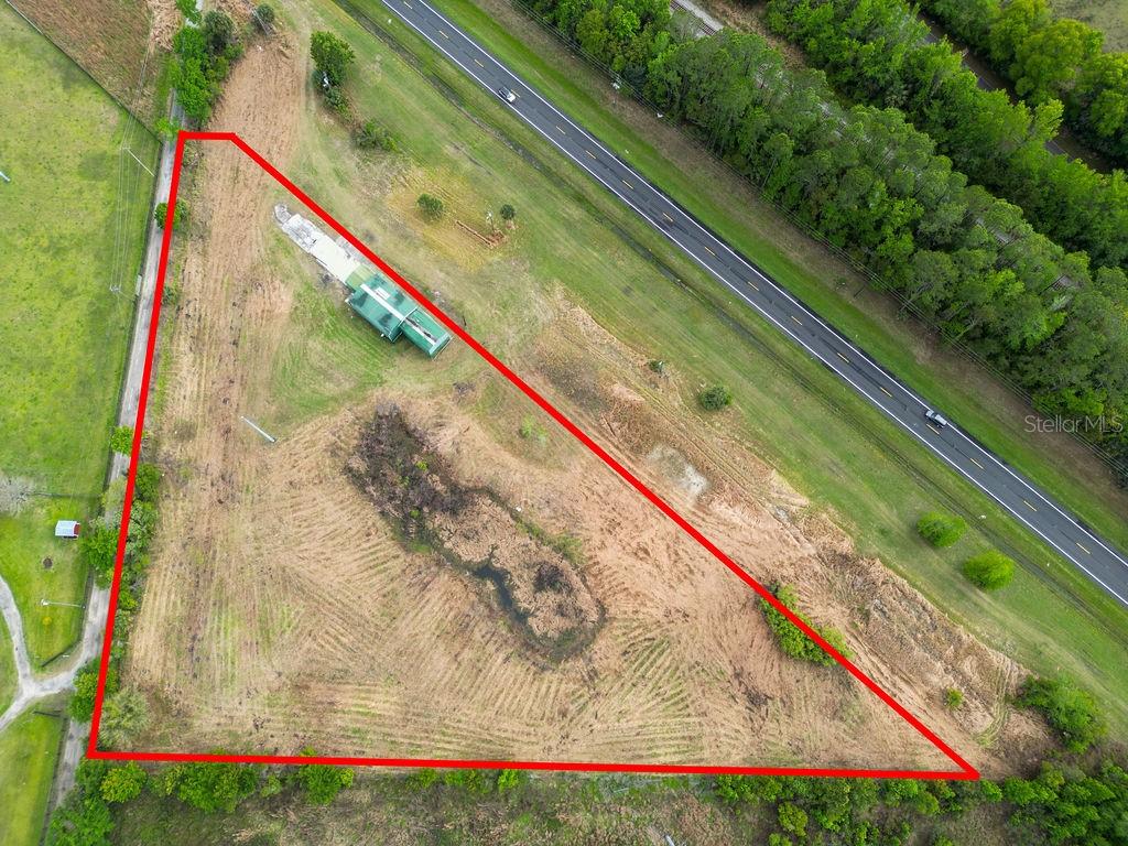 An aerial view shows a triangular plot of land with a small structure and pond — 6029 US HIGHWAY 17, DE LEON SPRINGS, FL
