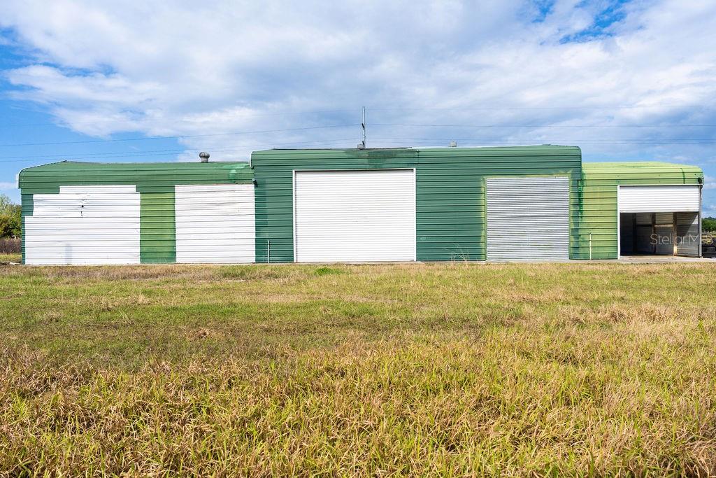 A green metal industrial building with multiple roll-up doors sits in a grassy field — 6029 US HIGHWAY 17, DE LEON SPRINGS, FL
